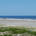 A wide view of a sandy beach with people and the ocean under a clear blue sky.