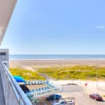 A sunny beach view from a balcony overlooking the ocean and sandy shore.